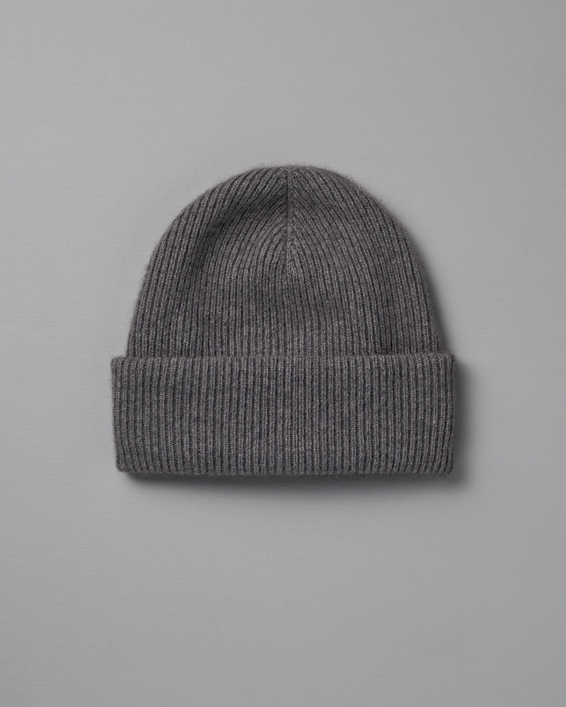 The Hinoki Beanie – Granite, a gray ribbed knit beanie with a folded brim, is laid flat on a light gray background.