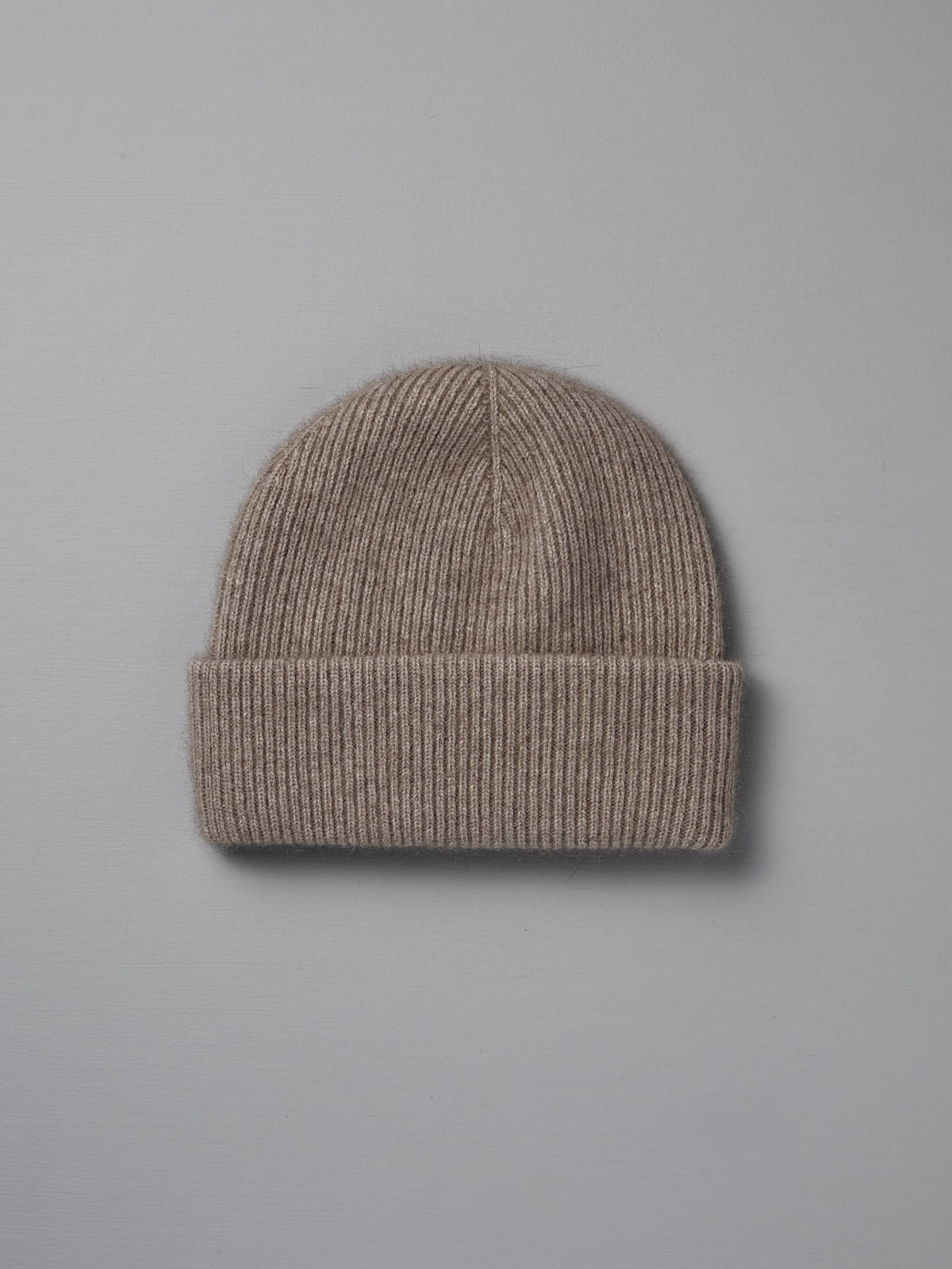 The Hinoki Beanie – Natural, a beige ribbed knit hat with a folded brim, is shown flat on a light gray background.