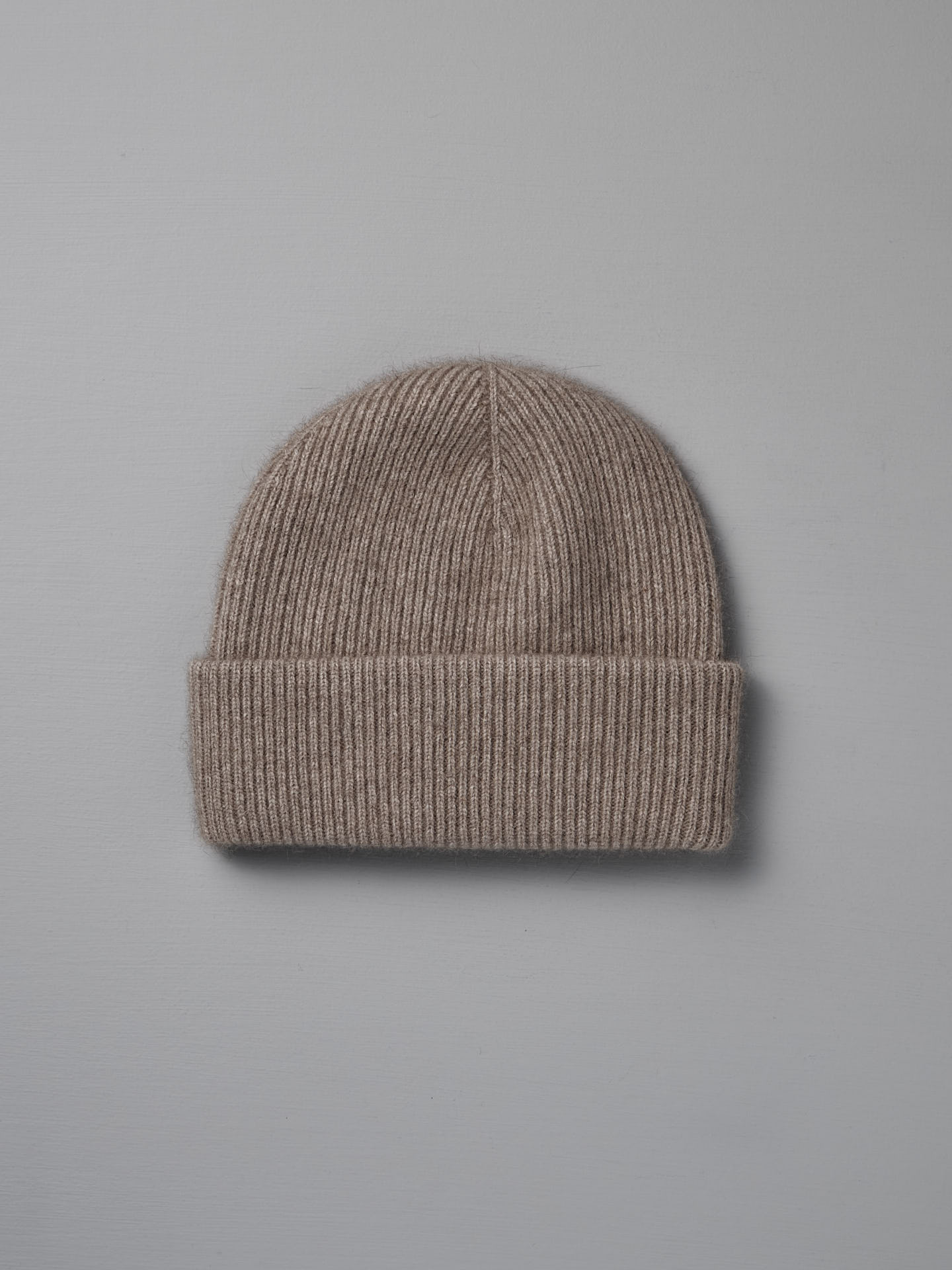 The Hinoki Beanie – Natural, a beige ribbed knit hat with a folded brim, is shown flat on a light gray background.
