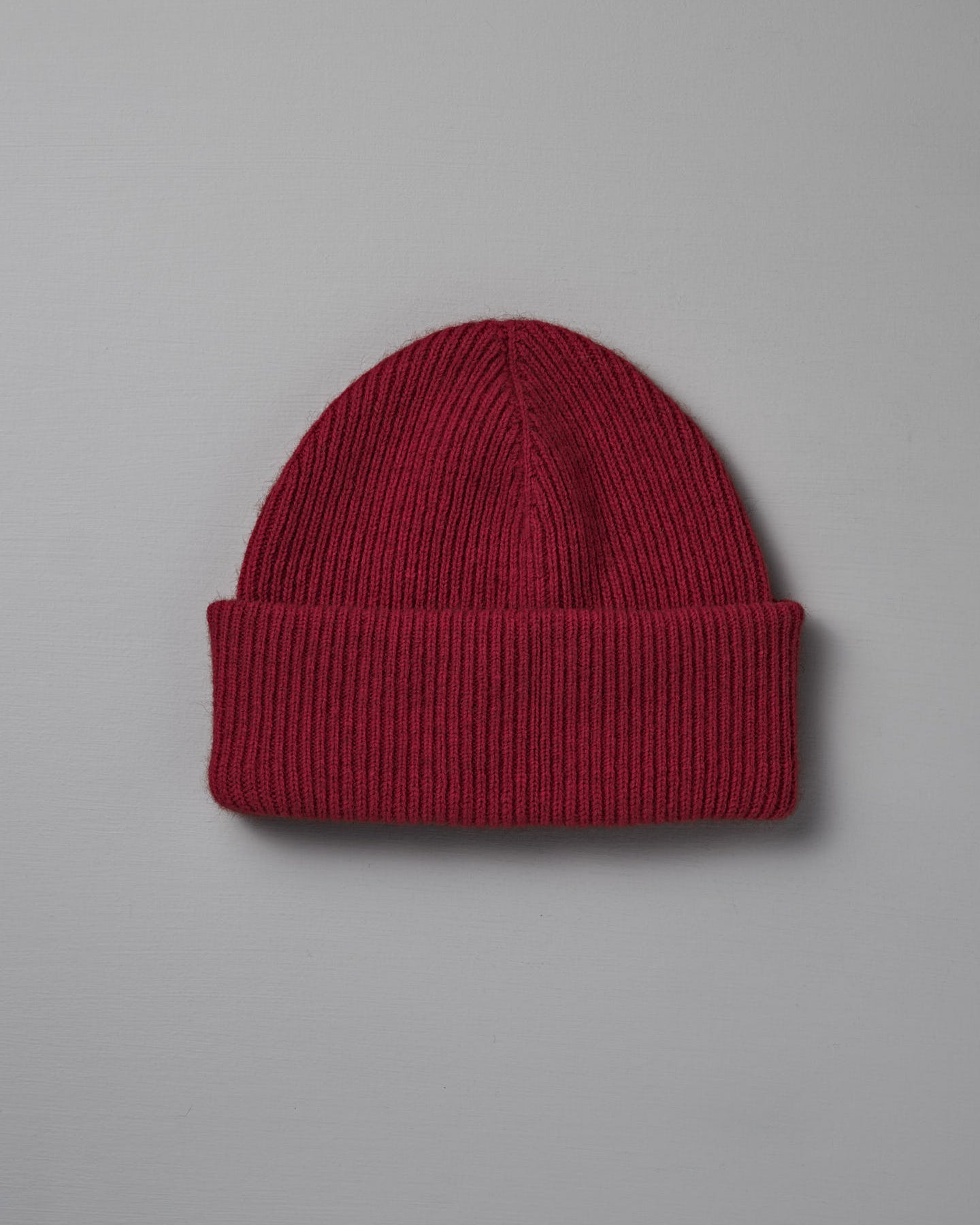 The Hinoki Beanie – Poppy, a red knit hat with a folded brim, is displayed on a plain light gray background.