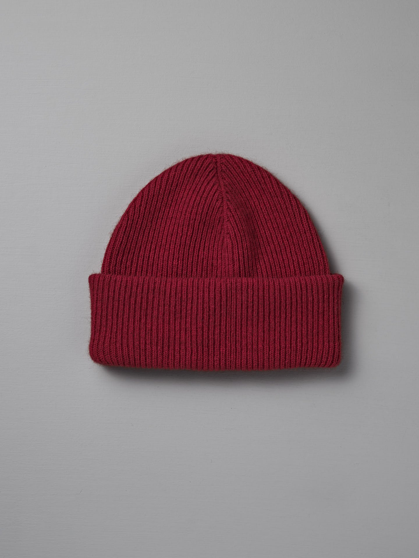 The Hinoki Beanie – Poppy, a red knit hat with a folded brim, is displayed on a plain light gray background.