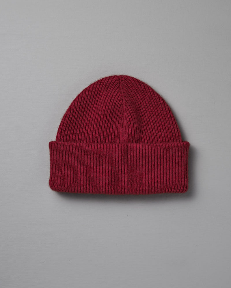 The Hinoki Beanie – Poppy, a red knit hat with a folded brim, is displayed on a plain light gray background.