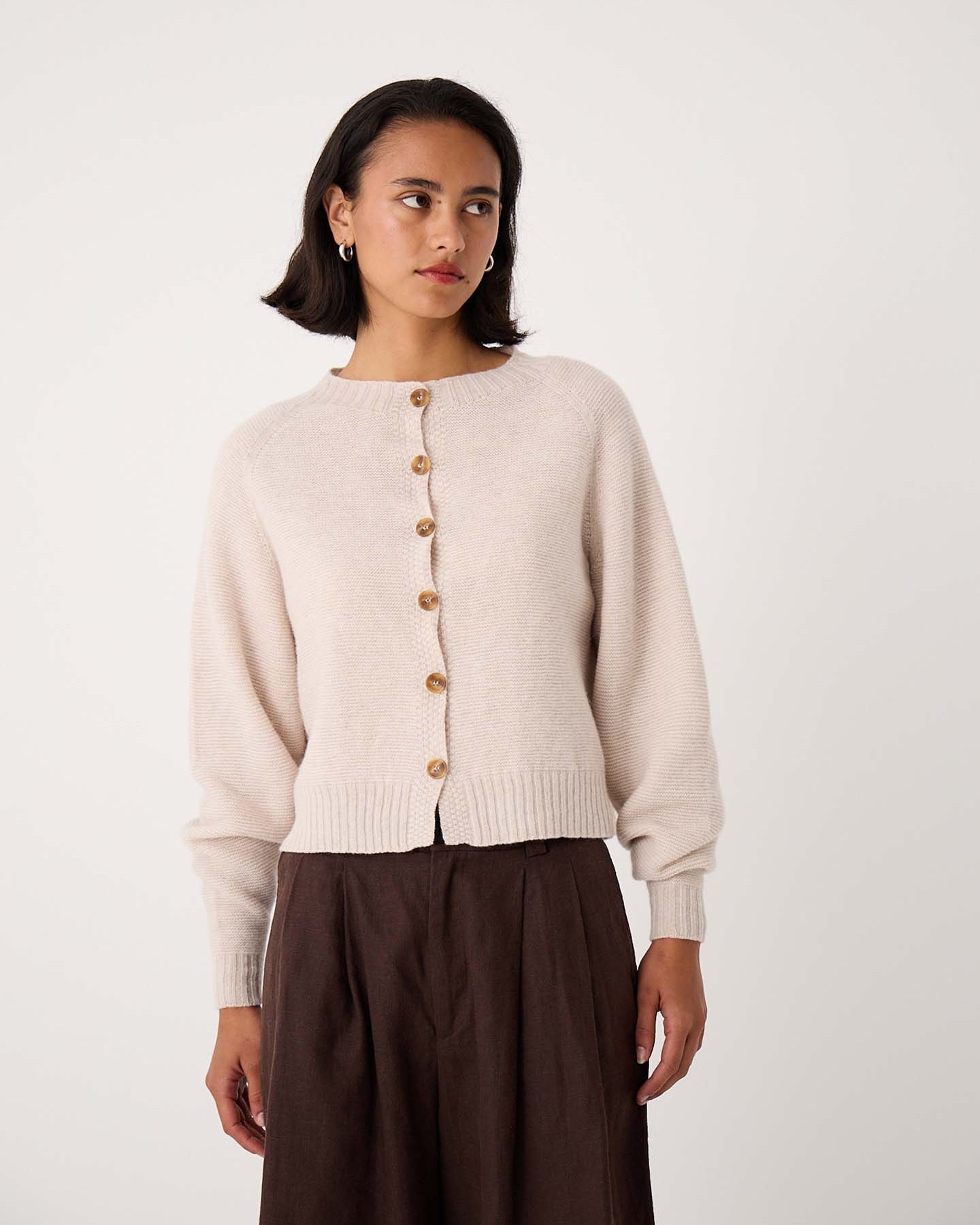 A woman wearing a Loft Cardigan – Creme and a dark brown skirt stands against a plain white background.