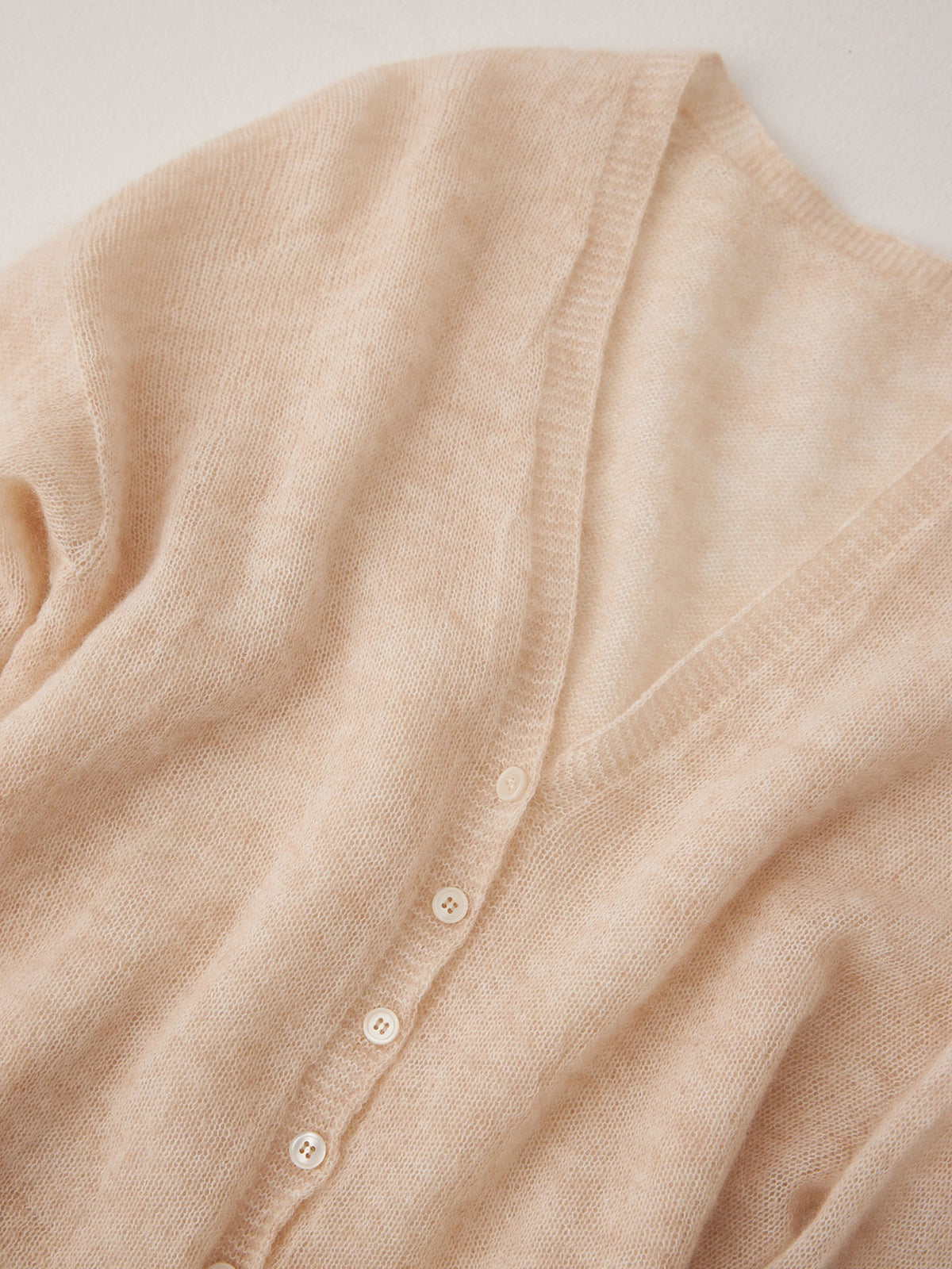The Mist Cardigan – Creme is a beige, soft-textured, cropped cardigan with a relaxed fit, V-neckline, and white buttons, shown flat on a light surface.