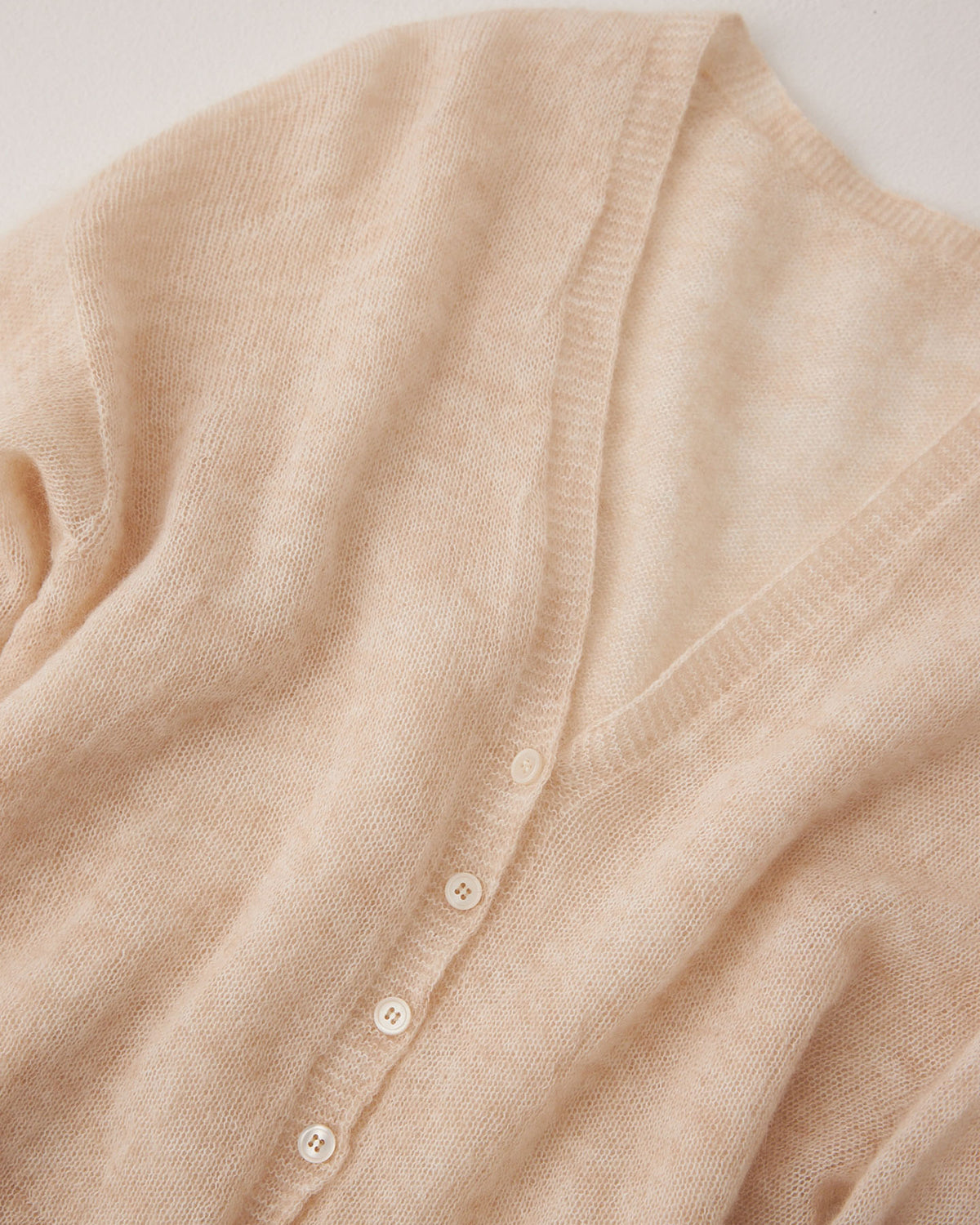The Mist Cardigan – Creme is a beige, soft-textured, cropped cardigan with a relaxed fit, V-neckline, and white buttons, shown flat on a light surface.