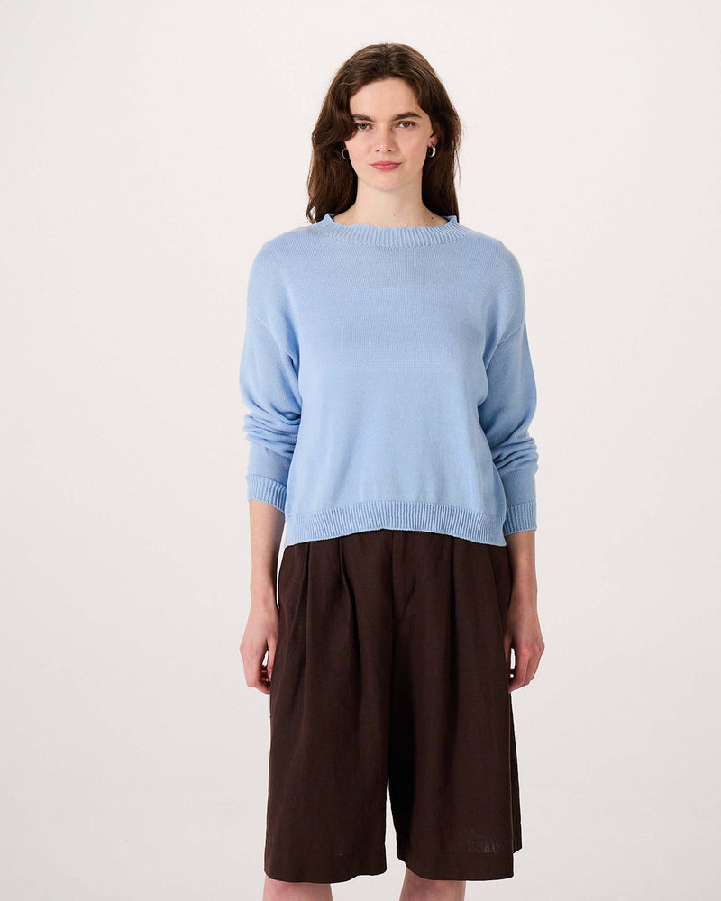 Woman wearing a light blue sweater and loose brown knee-length shorts, standing against a plain white background.