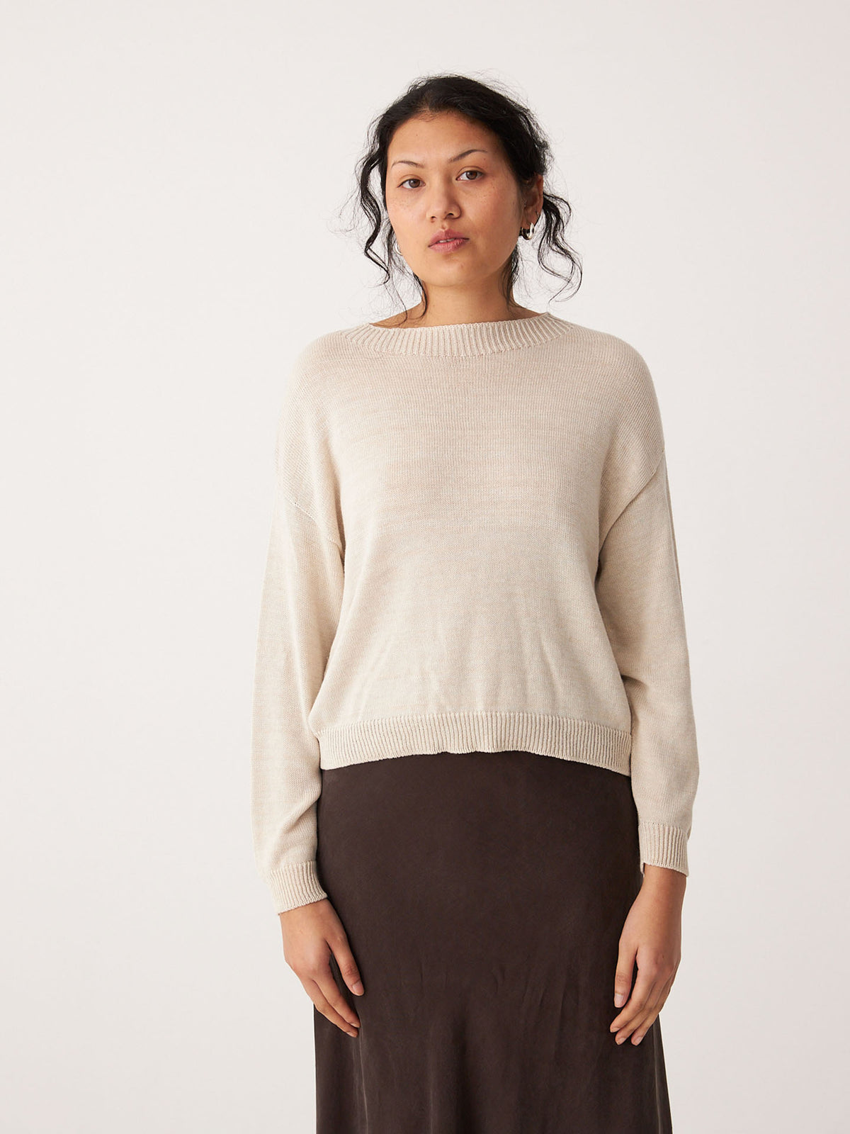A person stands against a plain light background, wearing the Pebble Knit – Creme sweater and a dark skirt, looking directly at the camera.