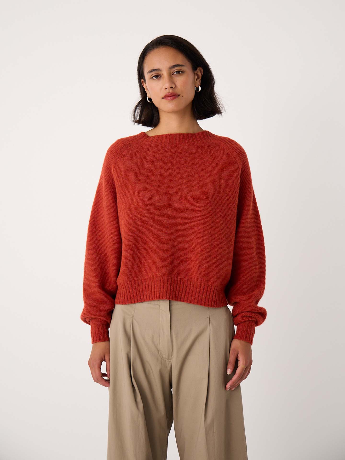 A petite woman stands facing forward, wearing the Poet Knit – Amber in a relaxed fit with beige pants against a plain white background.