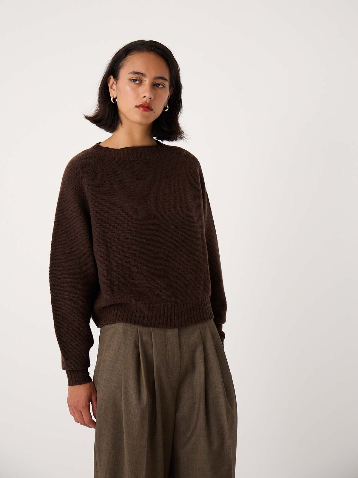 A petite person wears the Poet Knit – Cocoa sweater with relaxed fit, olive green trousers, standing against a plain white background.