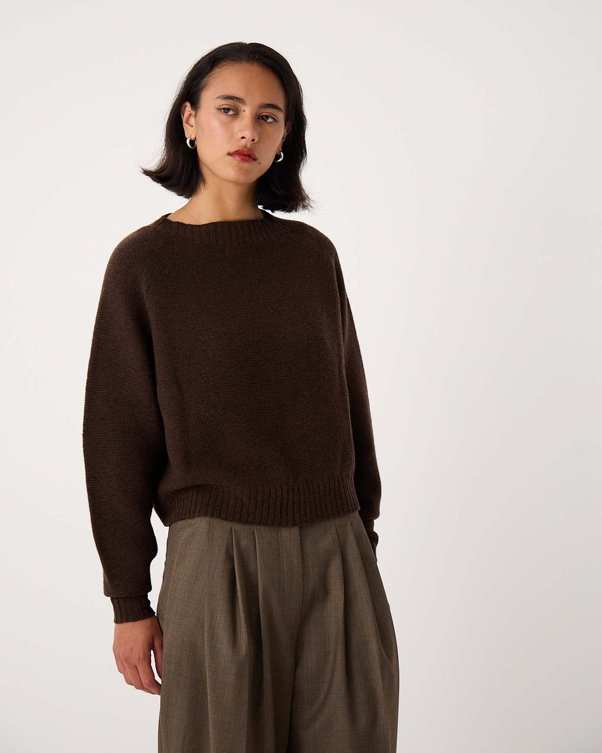 A petite person wears the Poet Knit – Cocoa sweater with relaxed fit, olive green trousers, standing against a plain white background.