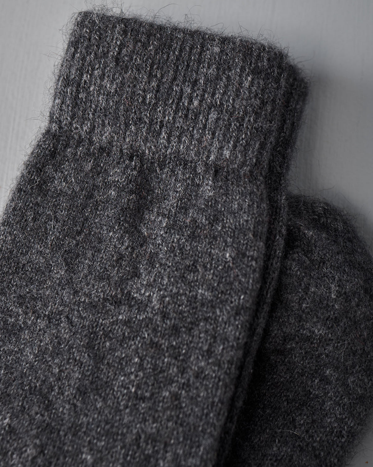 A close-up of Francie’s Possum Merino Socks – Charcoal, made from thick dark gray wool, shown on a light gray surface. Available in small, medium, and large UK/US/EUR sizes.