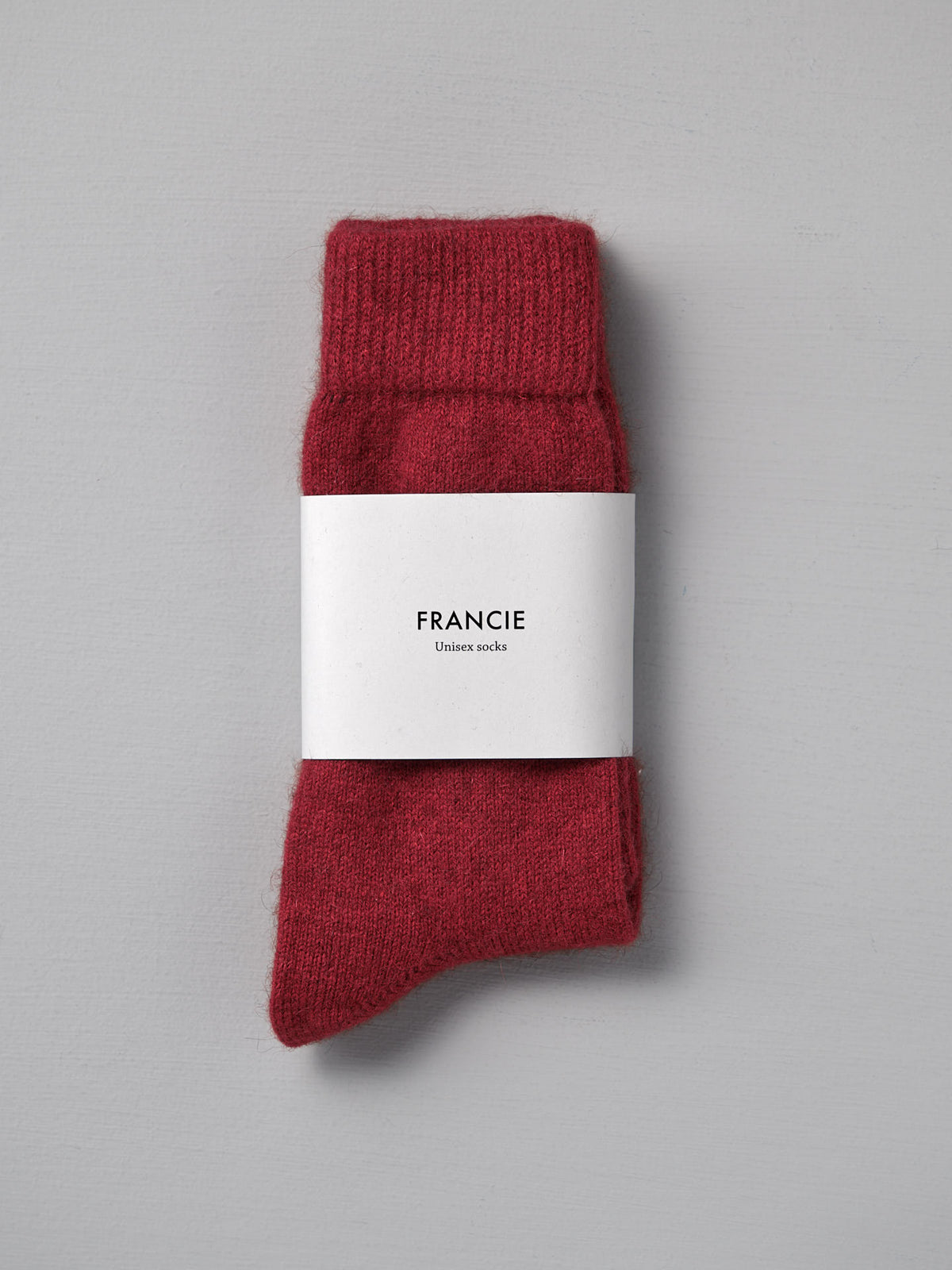 A pair of Francie Possum Merino Socks – Crimson in size Small, folded with a white &quot;Francie Unisex socks&quot; label, placed on a light gray surface.