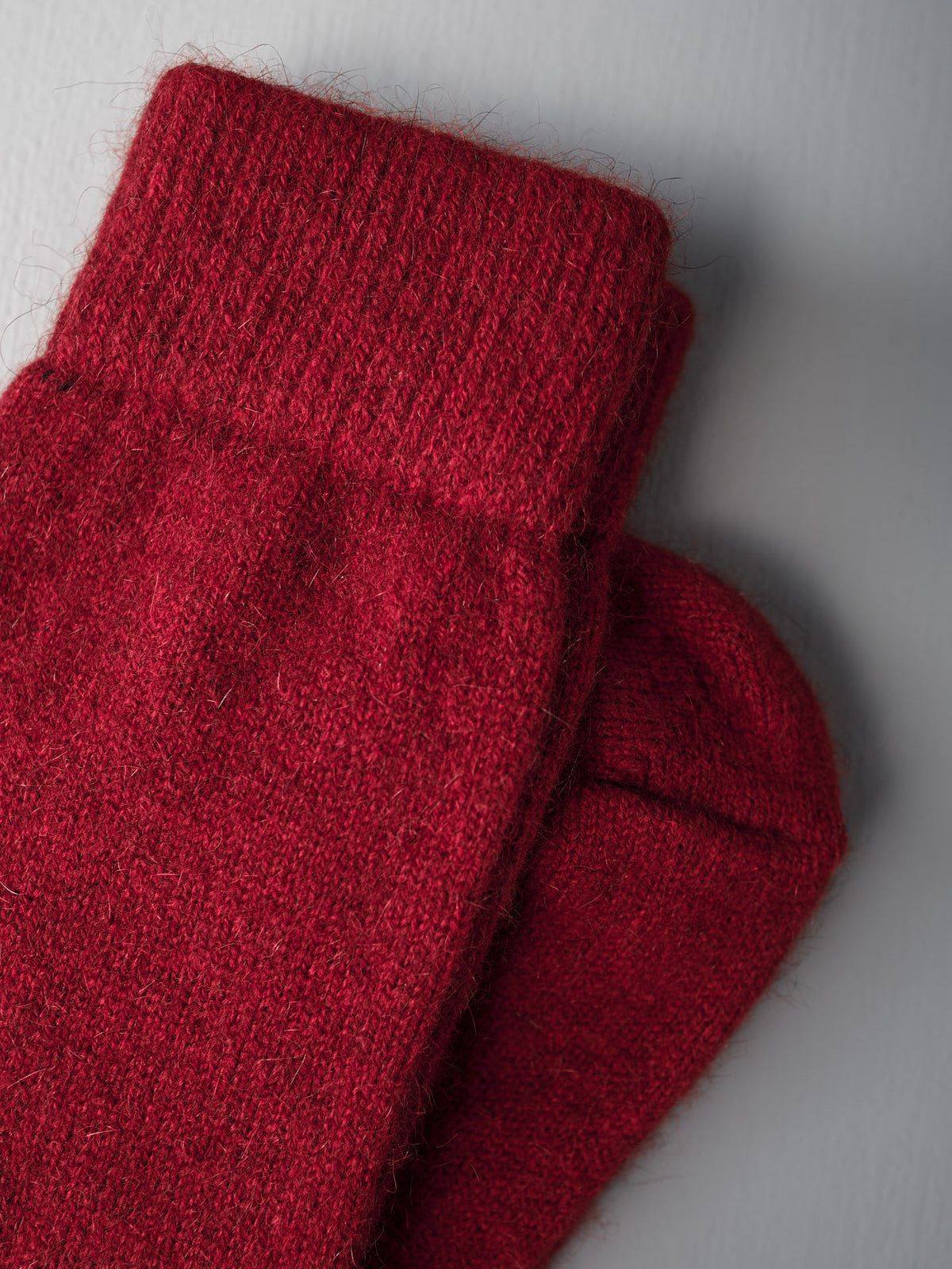 A pair of Francie Possum Merino Socks in crimson displayed on a light gray surface.