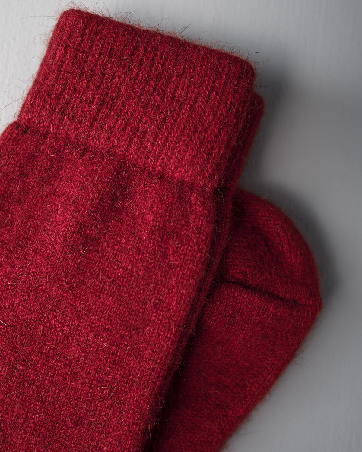 A pair of Francie Possum Merino Socks in crimson displayed on a light gray surface.