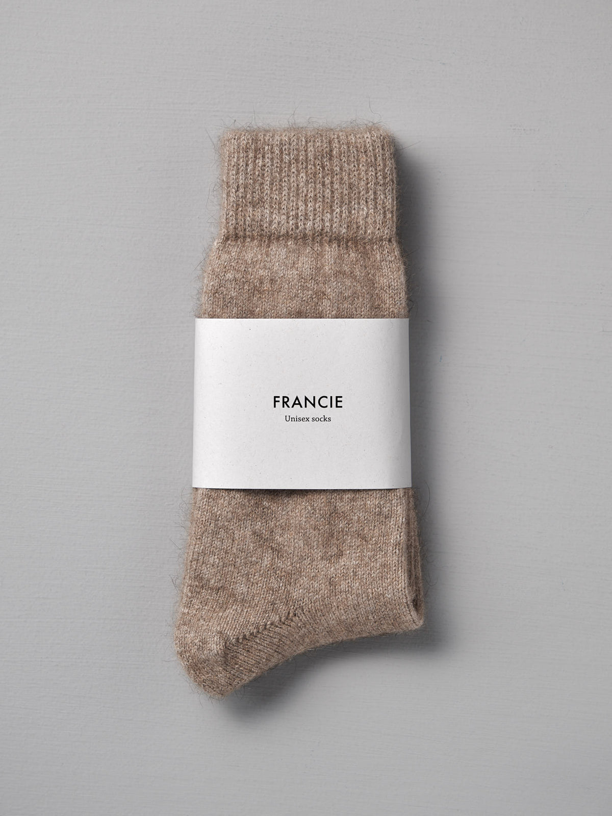 A pair of beige Francie Possum Merino Socks – Natural, neatly folded with a white &quot;Francie&quot; label on a plain grey background. Available in small, medium, and large with an easy-to-read size chart for EUR, UK, and US shoe sizes.