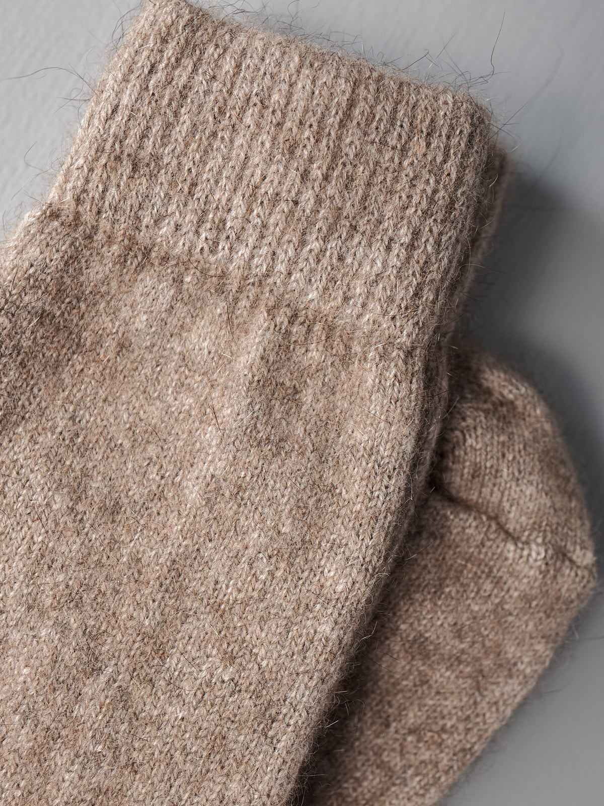 A close-up of two Francie Possum Merino Socks – Natural with ribbed cuffs on a gray surface, available in small, medium, and large sizes with an easy shoe size chart for EUR, UK, and US.