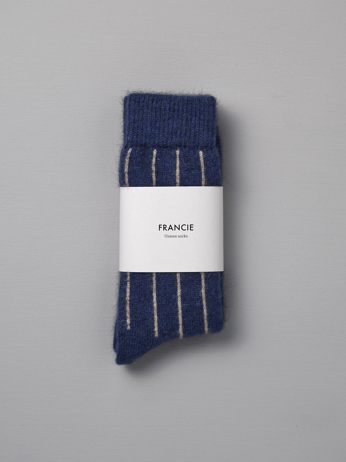 A folded pair of Francie Possum Merino Socks – Blue &amp; Natural Stripe, wrapped in branded packaging, sits on a light grey background—ideal for those needing easy size chart guidance in small, medium, or large.