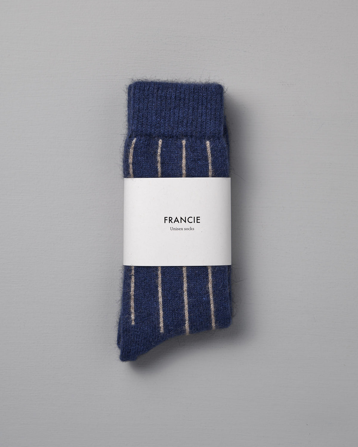 A folded pair of Francie Possum Merino Socks – Blue & Natural Stripe, wrapped in branded packaging, sits on a light grey background—ideal for those needing easy size chart guidance in small, medium, or large.