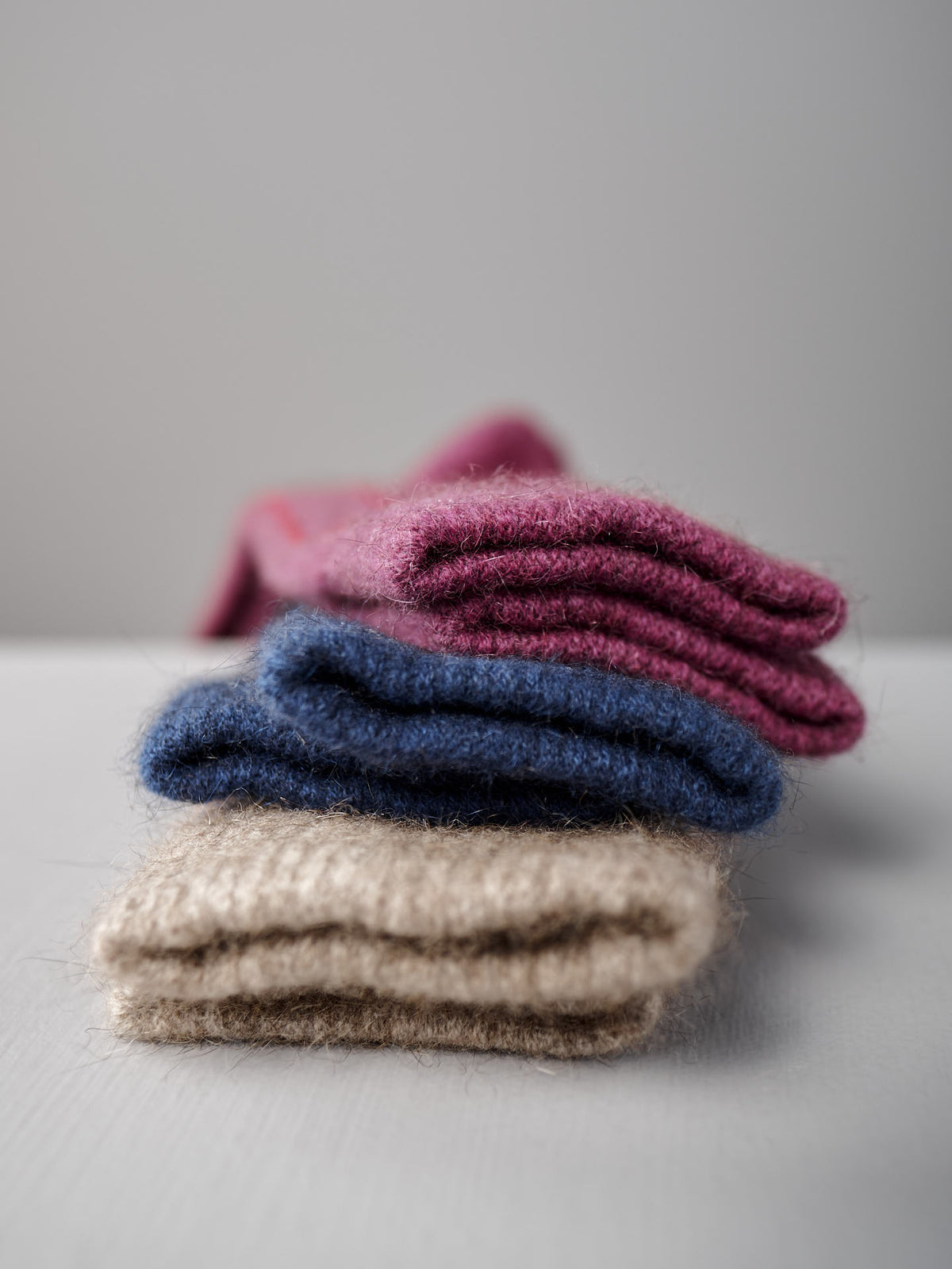Francie&#39;s Possum Merino Socks in Natural &amp; Poppy Stripe are displayed stacked on a white surface with a plain gray background.