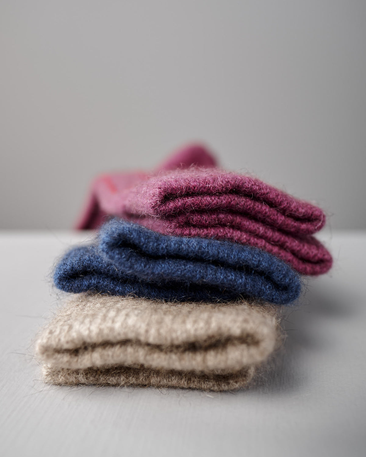 Francie's Possum Merino Socks in Natural & Poppy Stripe are displayed stacked on a white surface with a plain gray background.