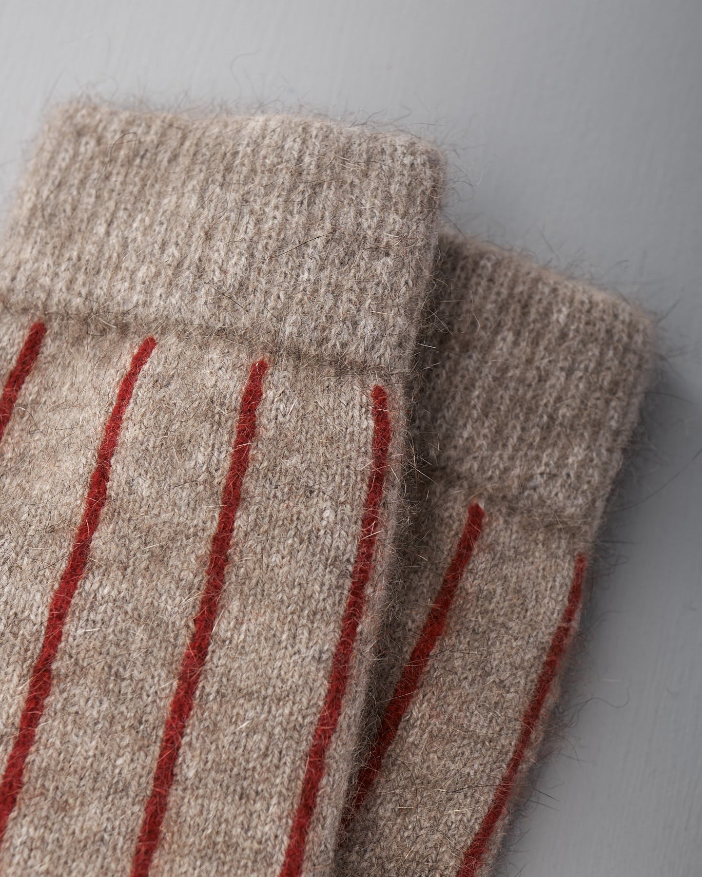 A pair of beige Possum Merino Socks by Francie with red stripes on a light gray background.