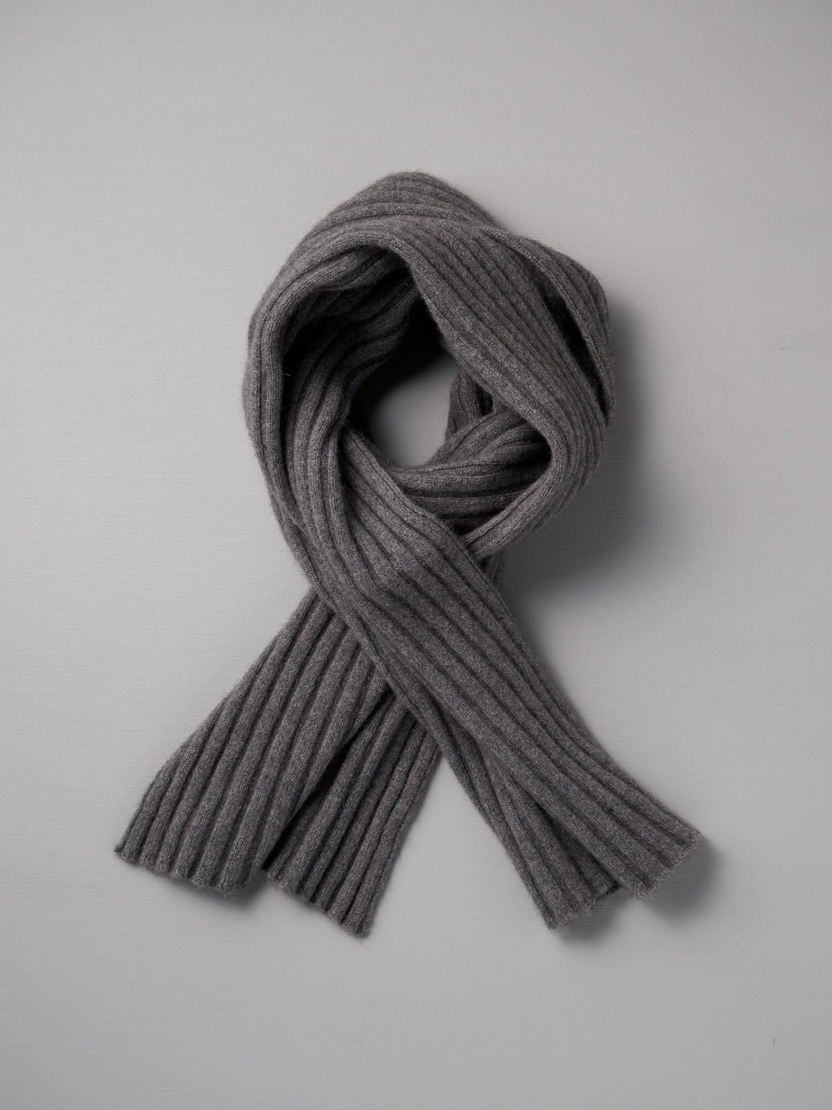 The Francie Ripple Scarf in Herb Green, 24cm wide at its widest point, is laid flat on a light gray background with its ends crossed over each other.
