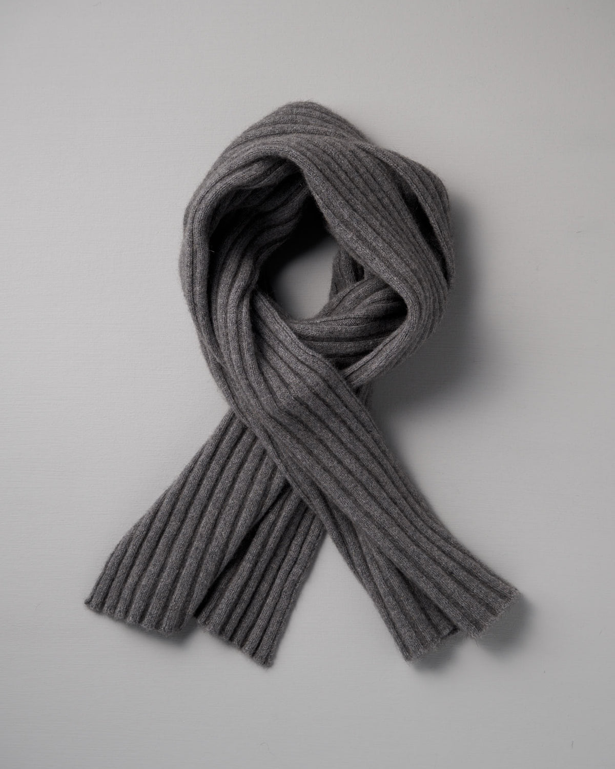The Francie Ripple Scarf in Herb Green, 24cm wide at its widest point, is laid flat on a light gray background with its ends crossed over each other.