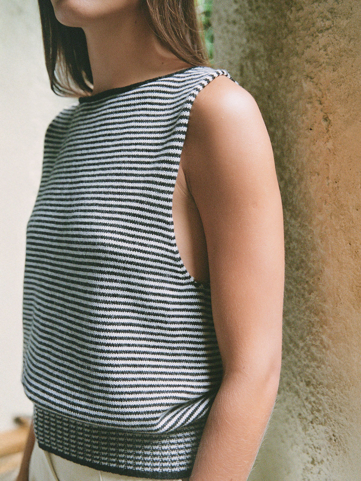 A person wearing the Francie Striped Star Vest in Black &amp; Creme stands by a textured wall, partially out of frame.