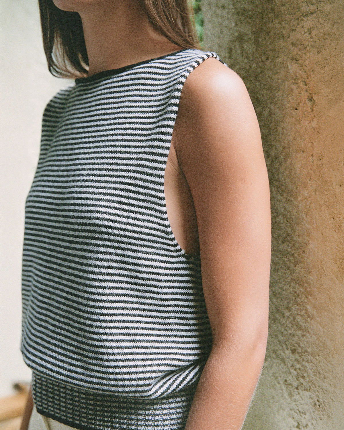 A person wearing the Francie Striped Star Vest in Black & Creme stands by a textured wall, partially out of frame.