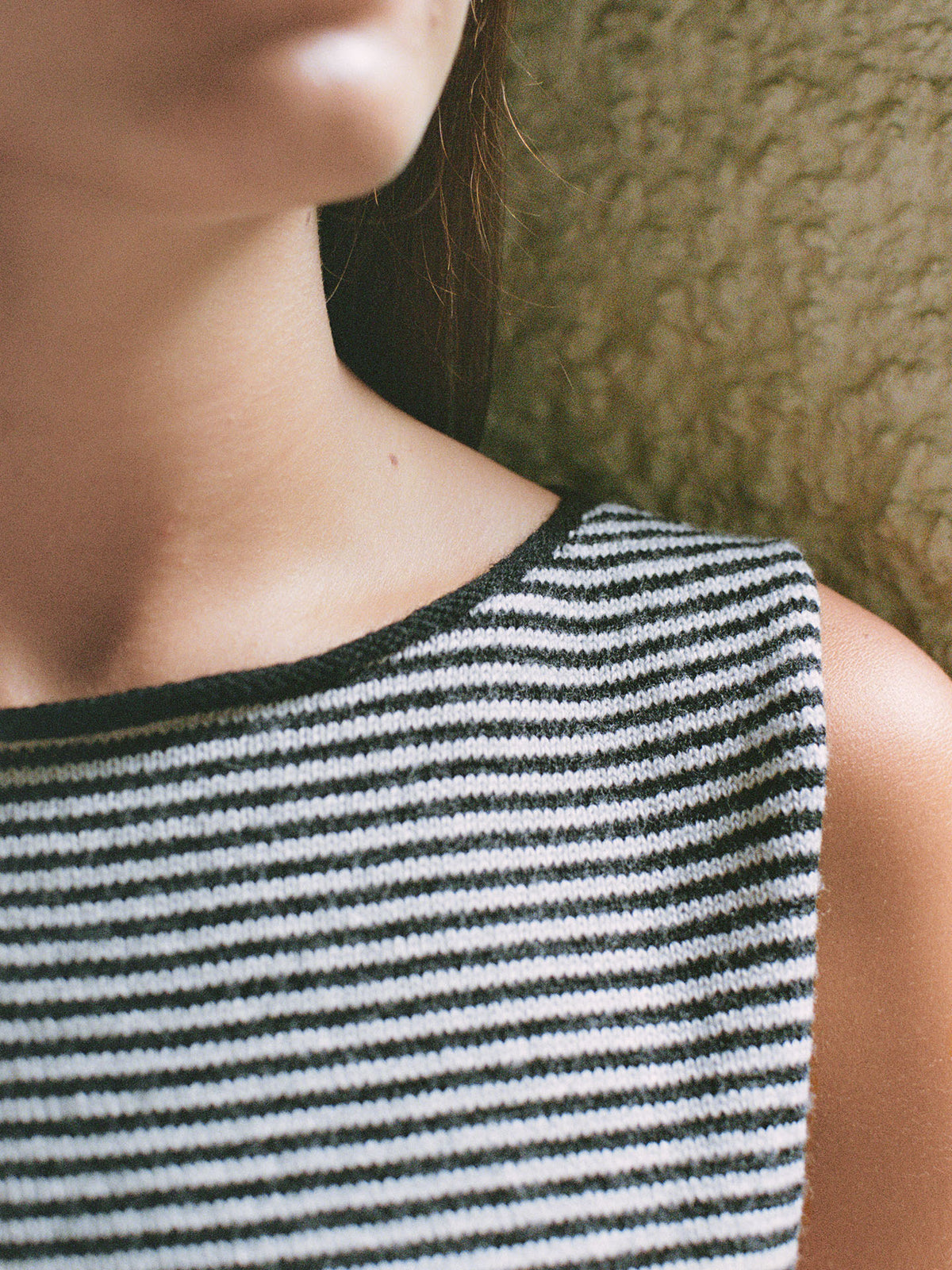 Close-up of a person wearing Francie&#39;s Striped Star Vest in Black &amp; Creme, a sleeveless, relaxed-fit top, against a textured background.