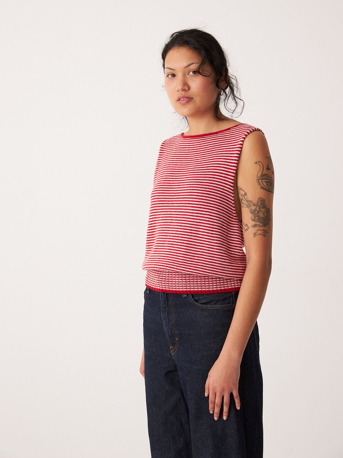A petite dark-haired person wears the Francie Striped Star Vest – Cherry &amp; Creme with relaxed fit dark jeans, standing against a plain light background.