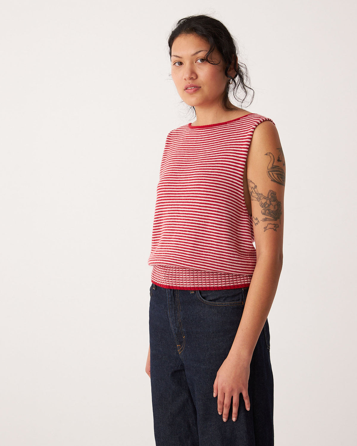 A petite dark-haired person wears the Francie Striped Star Vest – Cherry & Creme with relaxed fit dark jeans, standing against a plain light background.