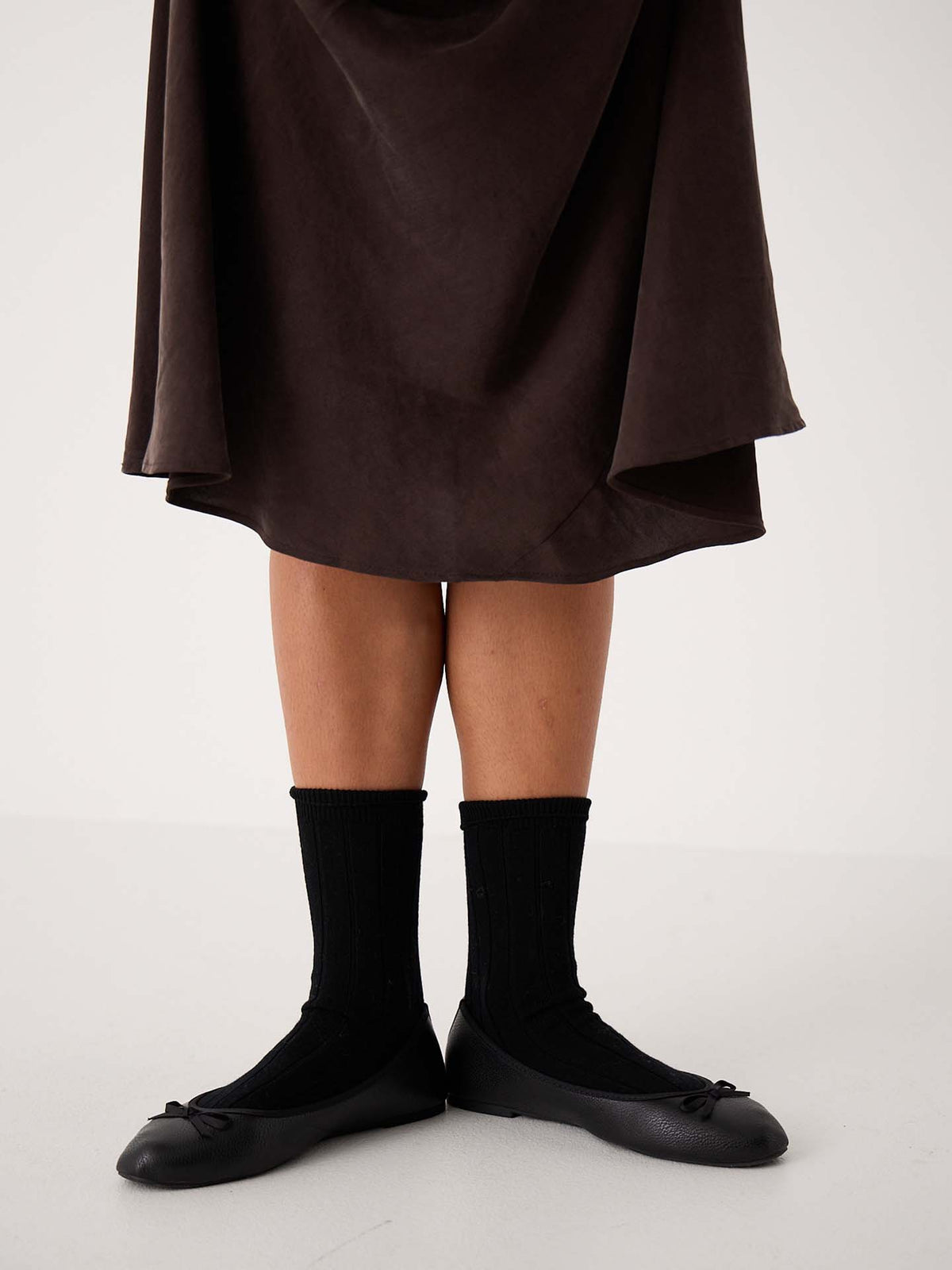 A person wearing a dark skirt, Tip Toe Crew Socks – Black & Chestnut Trim, and black ballet flats stands against a plain background—ideal for displaying shoe sizes in small, medium, or large (EU/UK/US).