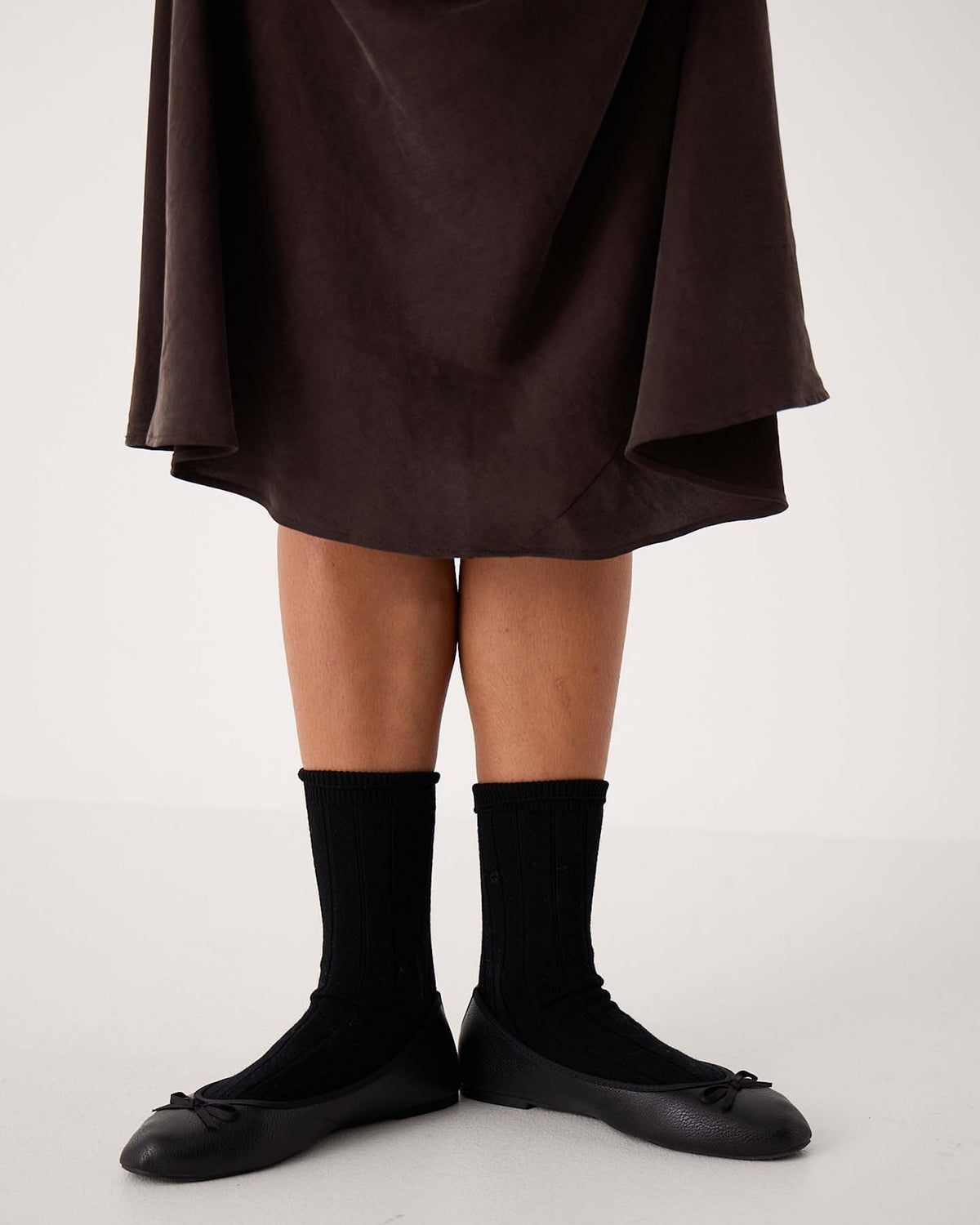A person wearing a dark skirt, Tip Toe Crew Socks – Black & Chestnut Trim, and black ballet flats stands against a plain background—ideal for displaying shoe sizes in small, medium, or large (EU/UK/US).
