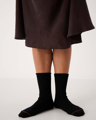 A person stands on a white floor wearing Tip Toe Crew Socks – Black & Chestnut Trim and a dark brown skirt; only legs and feet are visible, ideal for displaying various shoe size chart options (small, medium, large in EU, UK, US sizes).
