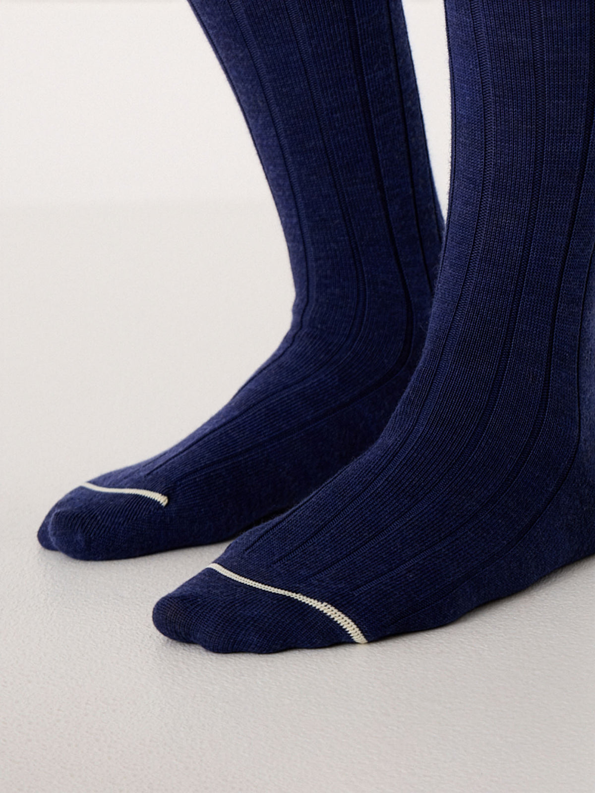 Close-up of feet wearing Tip Toe Crew Socks – Sapphire & Creme Trim, featuring ribbed navy blue fabric with a thin white accent near the toes, available in small, medium, and large sizes, standing on a light surface.