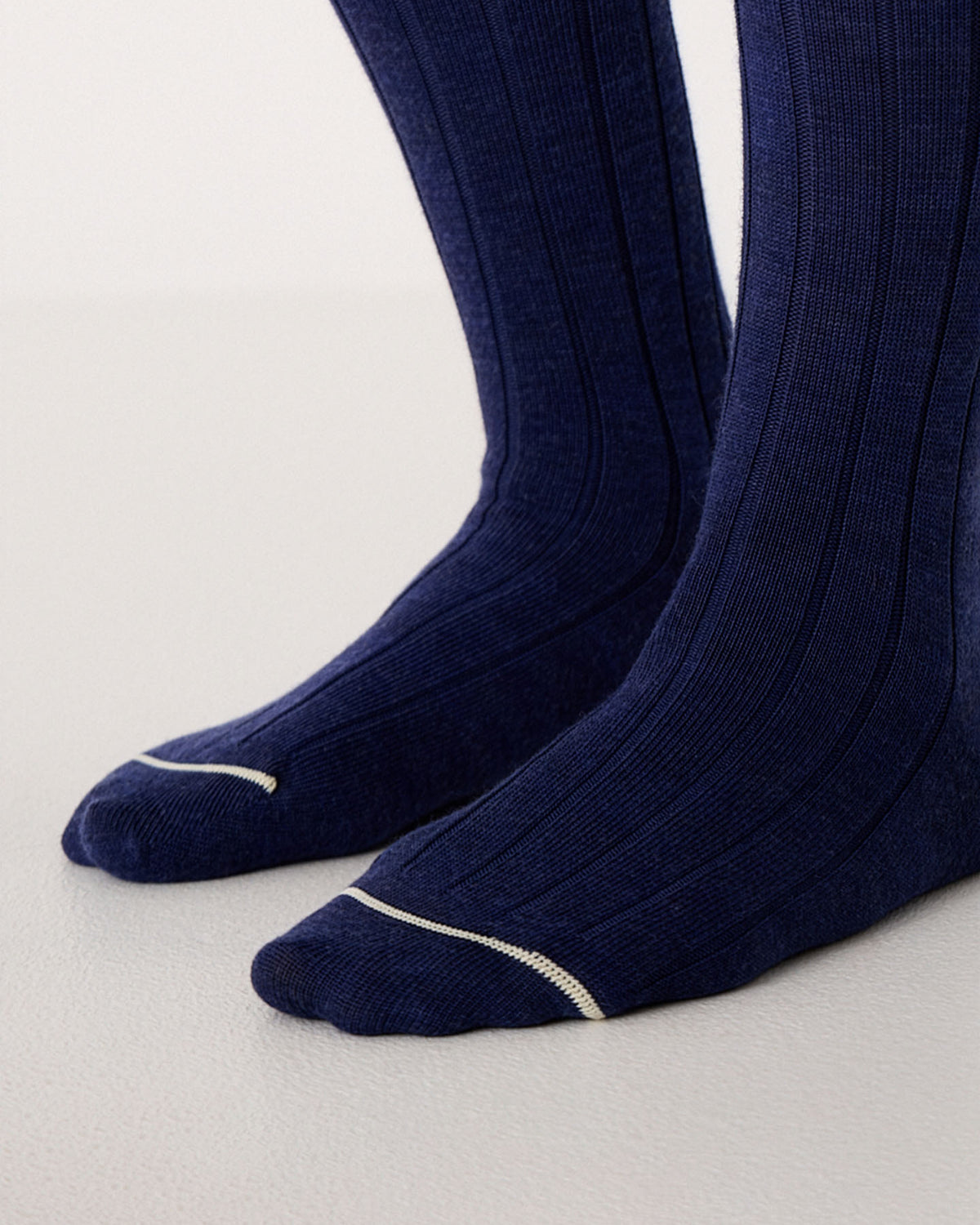 Close-up of feet wearing Tip Toe Crew Socks – Sapphire & Creme Trim, featuring ribbed navy blue fabric with a thin white accent near the toes, available in small, medium, and large sizes, standing on a light surface.