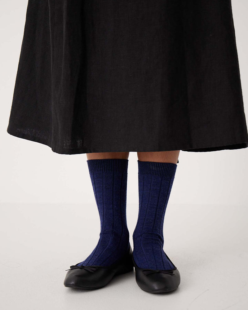 A person stands on a white floor wearing a long black skirt, black ballet flats, and Tip Toe Crew Socks in Sapphire with Creme Trim (available in sizes S, M, L) featuring a ribbed style.
