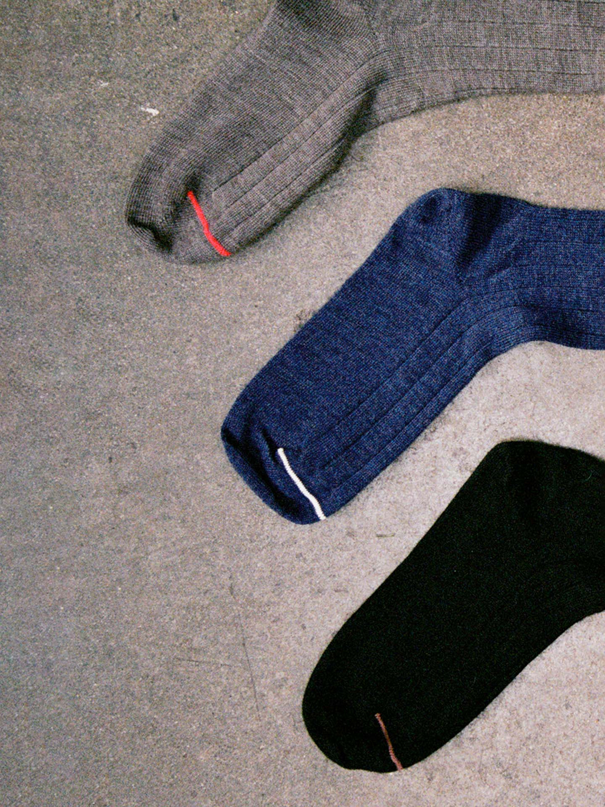 Tip Toe Crew Socks – Black & Chestnut Trim are laid out on concrete, each with a colored toe stitch. Available in small, medium, or large—see our shoe size chart for EU, UK, and US sizes.