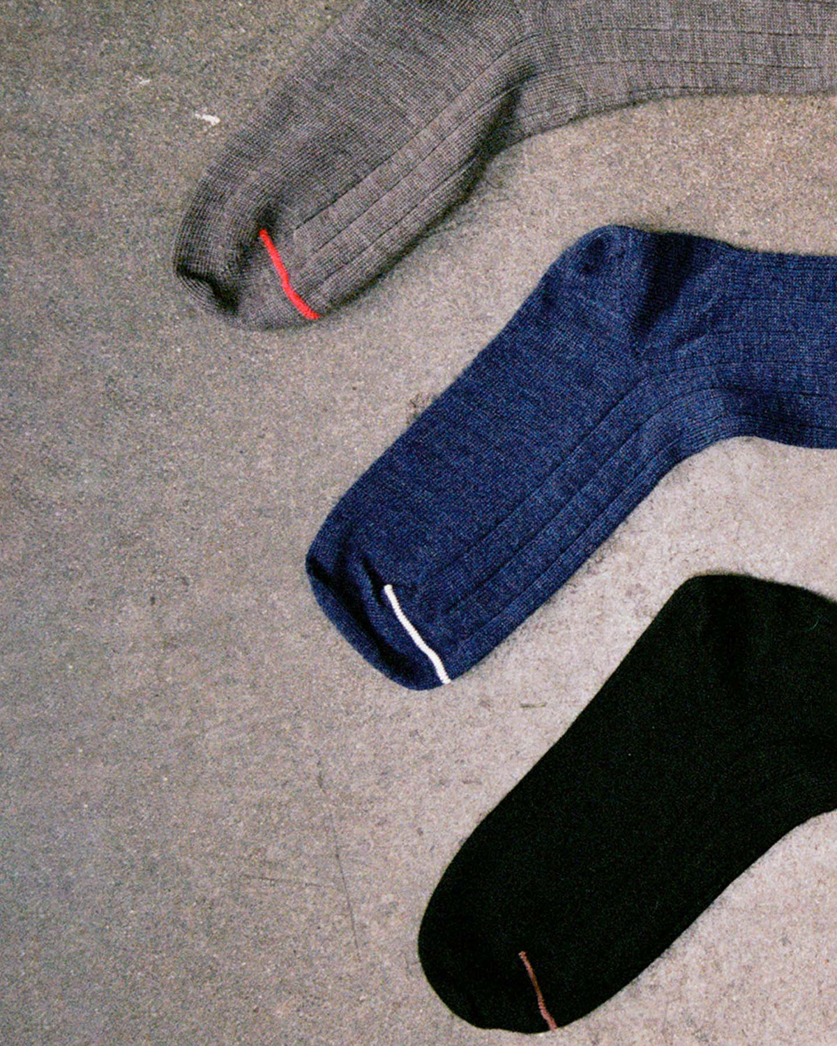 Tip Toe Crew Socks – Black & Chestnut Trim are laid out on concrete, each with a colored toe stitch. Available in small, medium, or large—see our shoe size chart for EU, UK, and US sizes.
