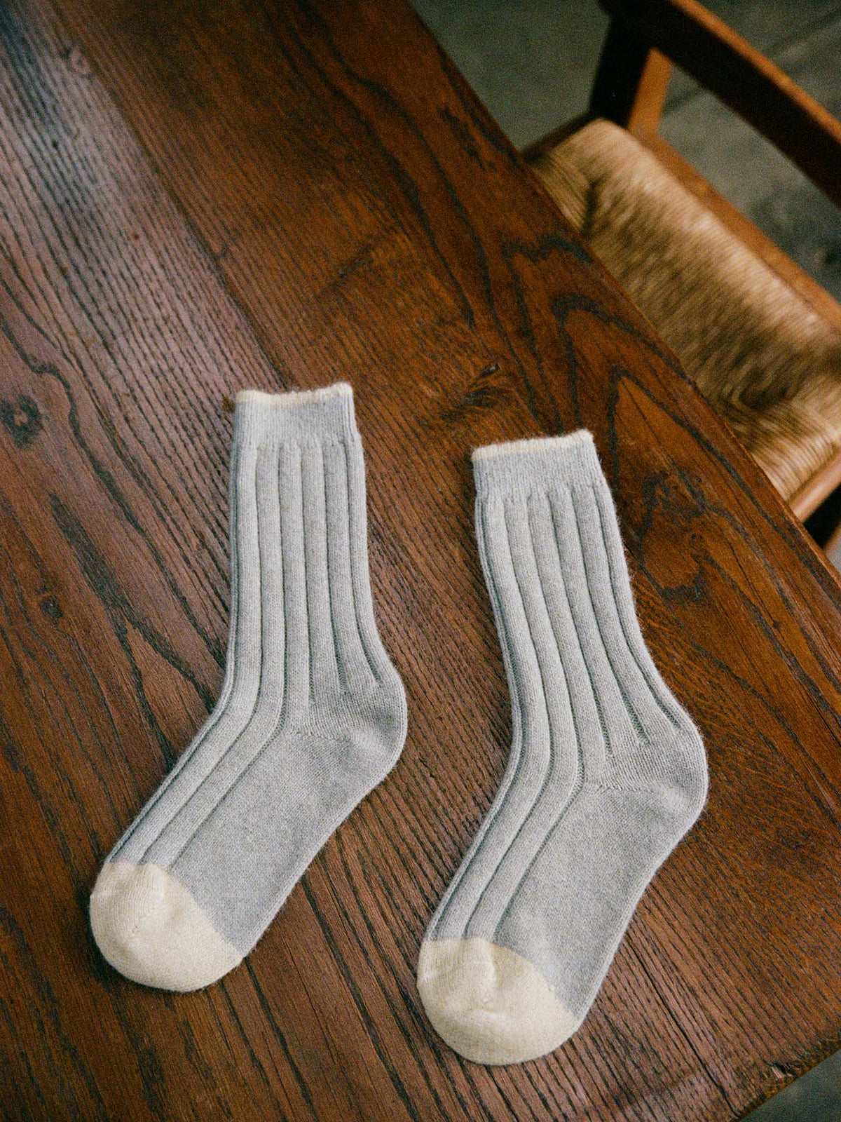 The Yin & Yang Socks – Pearl & Creme Toe, light gray with white toes and heels, rest on a wooden table beside a woven-seat chair—ideal for any size, with easy EU/UK/US fit through our shoe size chart.