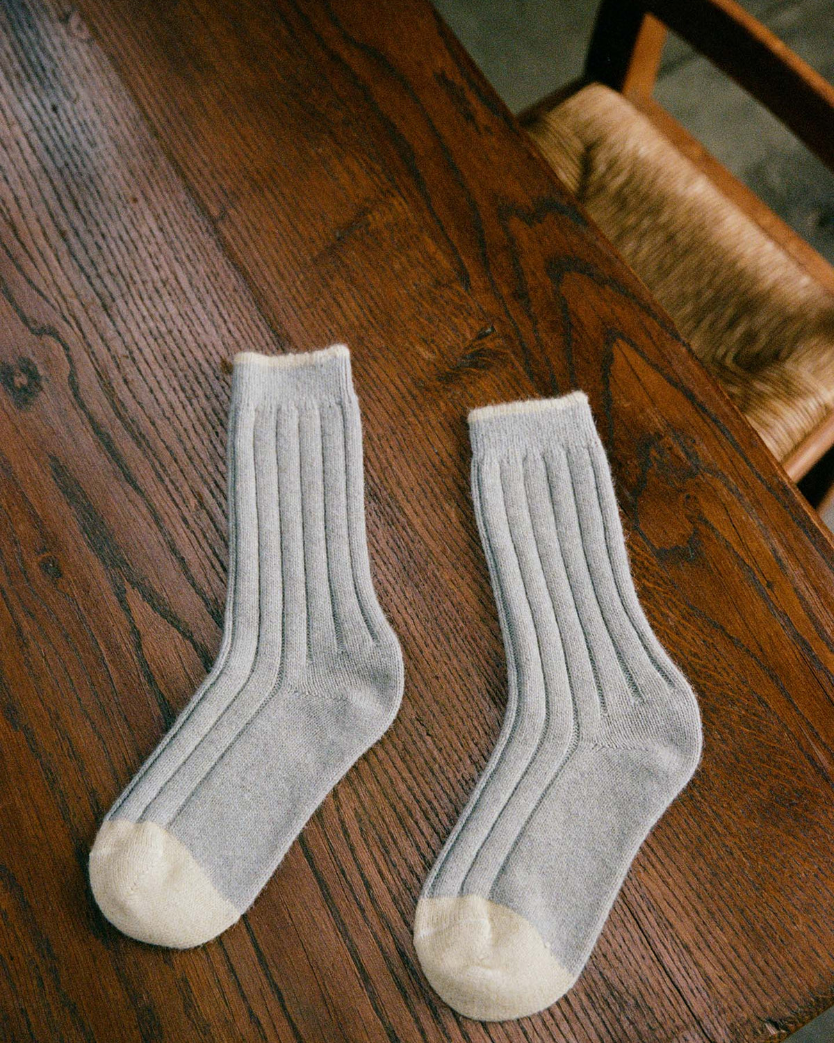 The Yin & Yang Socks – Pearl & Creme Toe, light gray with white toes and heels, rest on a wooden table beside a woven-seat chair—ideal for any size, with easy EU/UK/US fit through our shoe size chart.