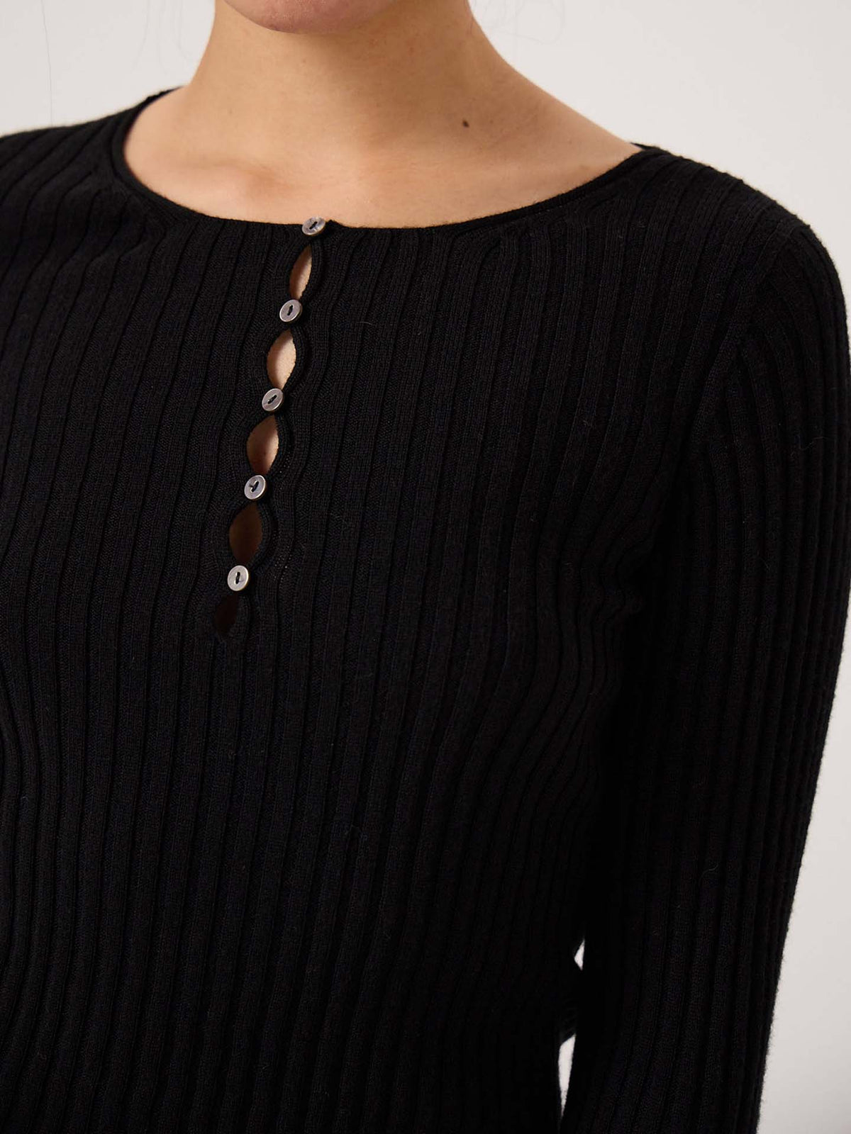 A person wearing the Form Top – Black, a chic petite fit featuring ribbed fabric, long sleeves, a round neckline, and partial button closure down the front.