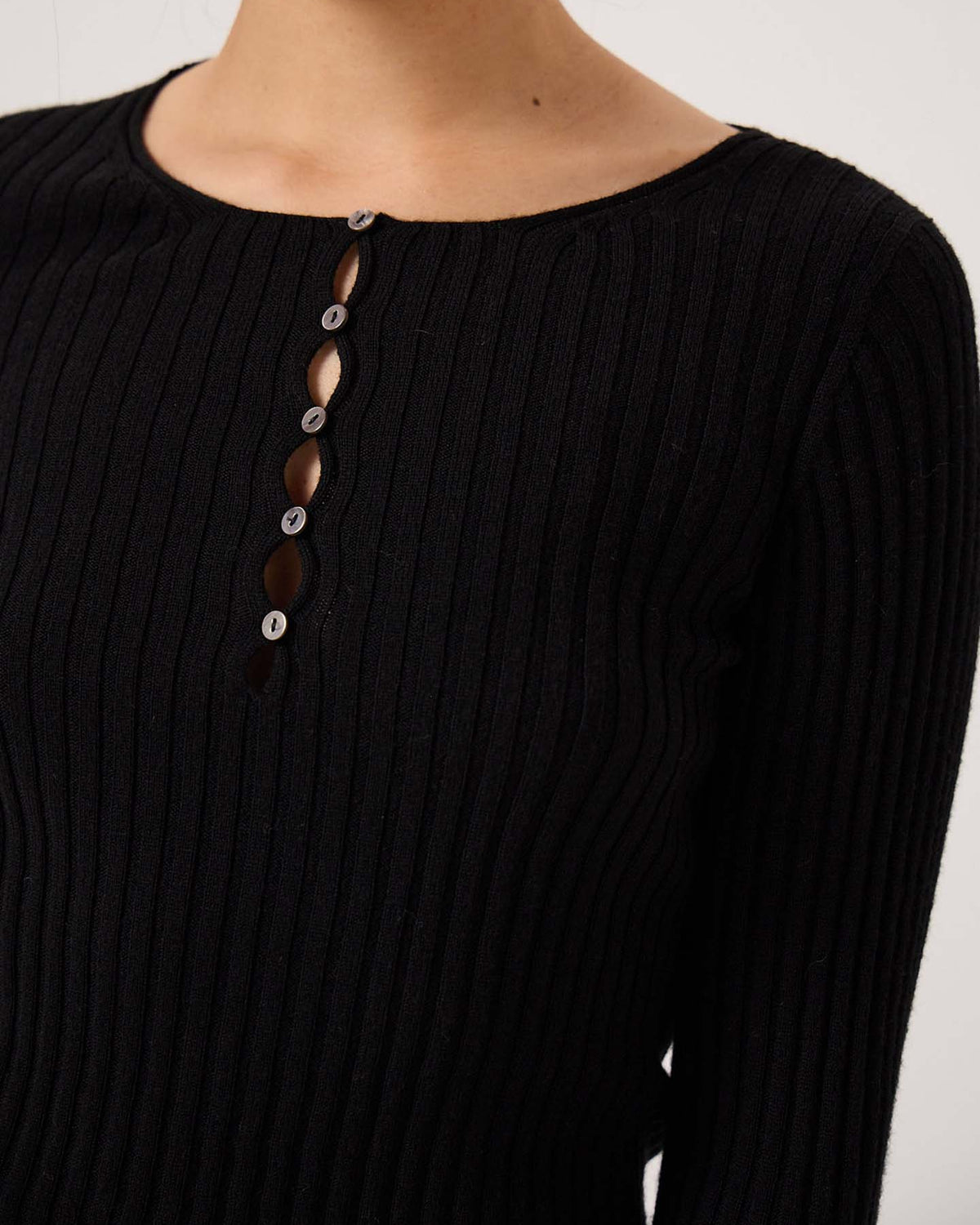 A person wearing the Form Top – Black, a chic petite fit featuring ribbed fabric, long sleeves, a round neckline, and partial button closure down the front.