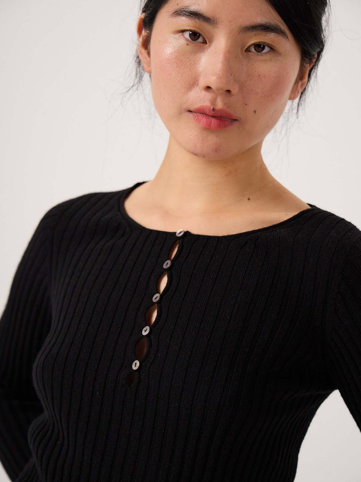 A person wears the Form Top – Black, a ribbed long-sleeve shirt with several buttons undone, standing against a plain light background.