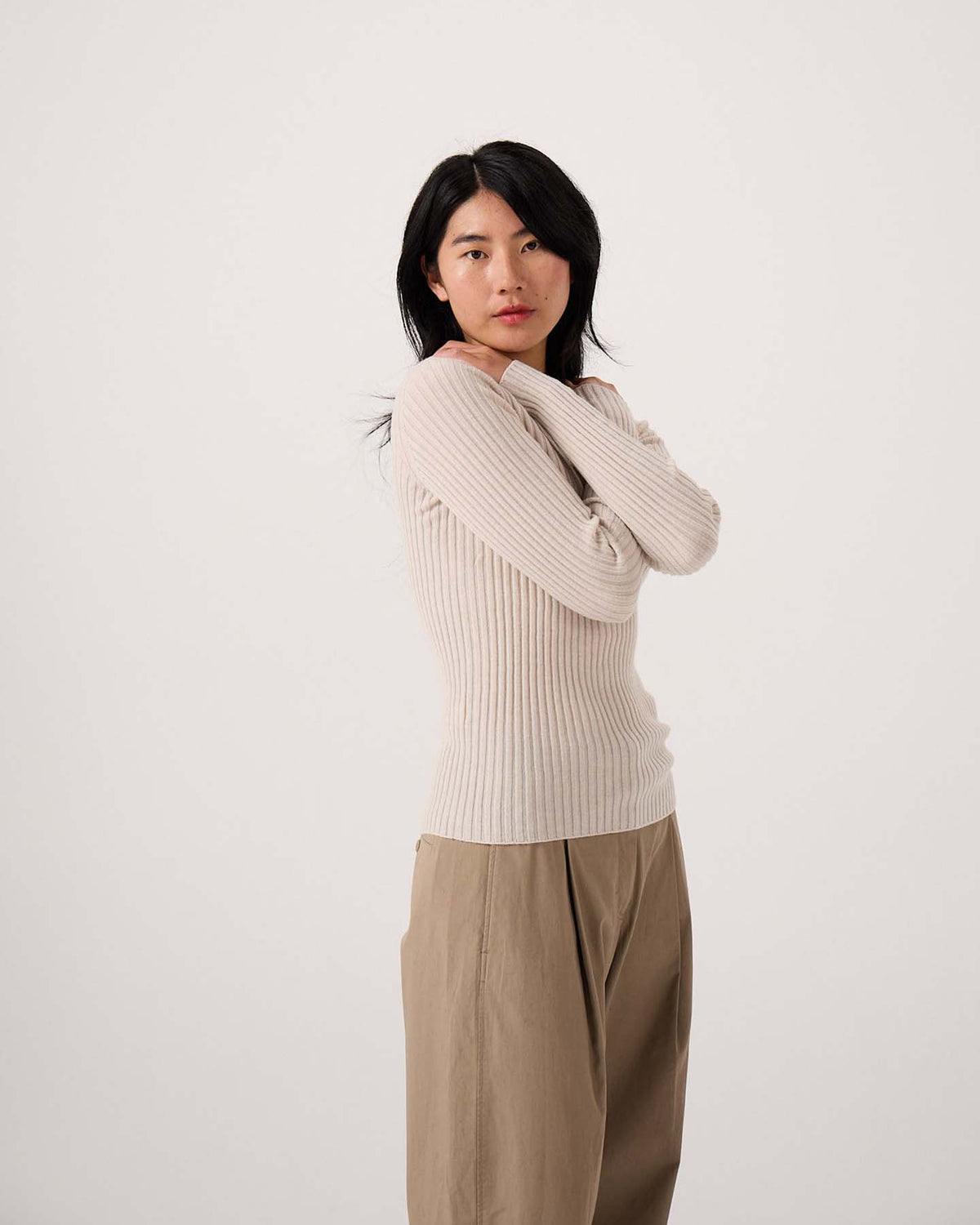 A petite woman with long black hair wears the Form Top – Ivory and loose tan pants, standing against a plain white background with her arms crossed.