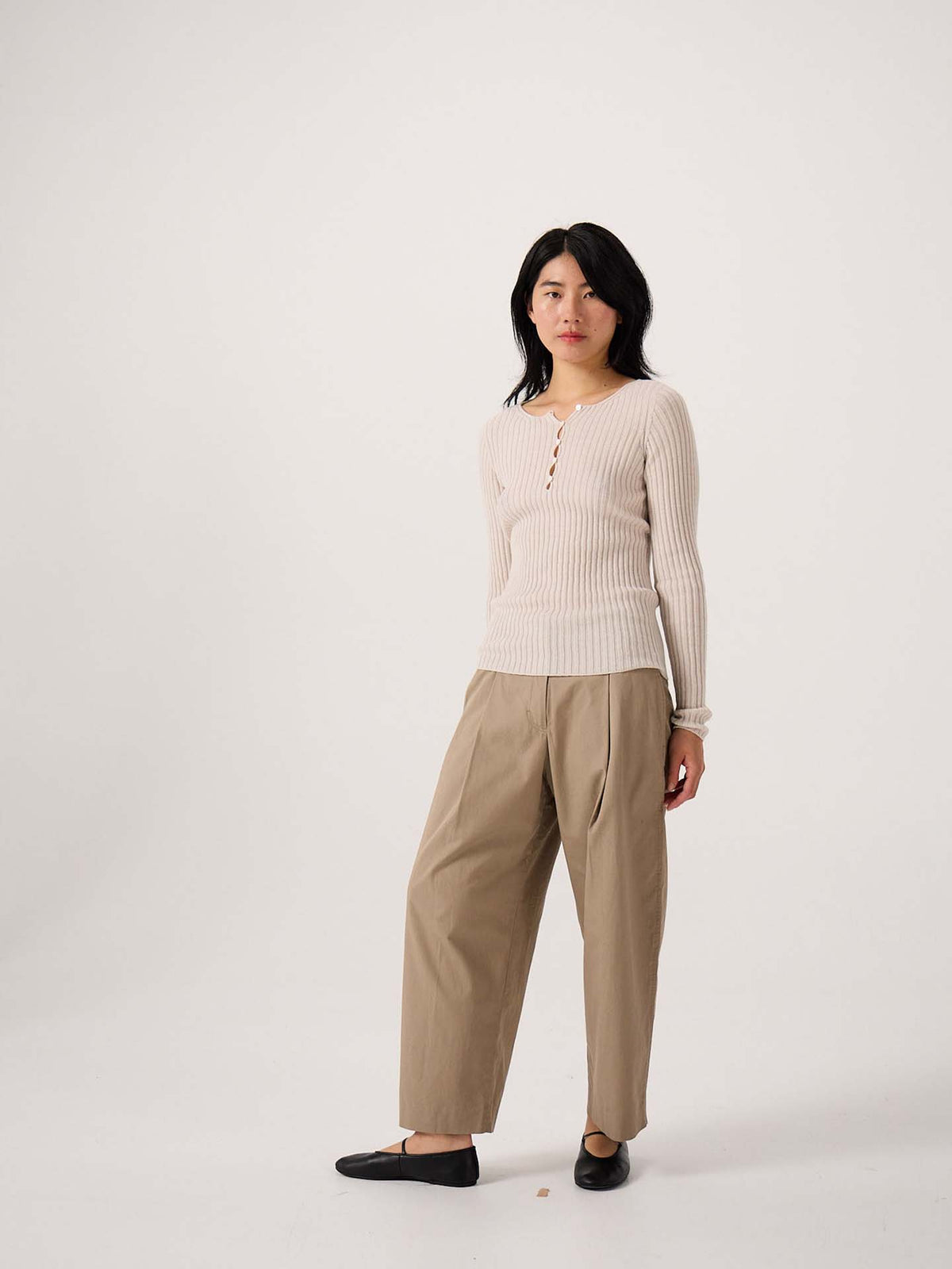 A petite person stands against a plain background, wearing the Form Top – Ivory, tan wide-leg trousers, and black flats.