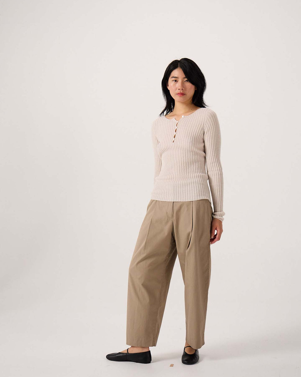 A petite person stands against a plain background, wearing the Form Top – Ivory, tan wide-leg trousers, and black flats.