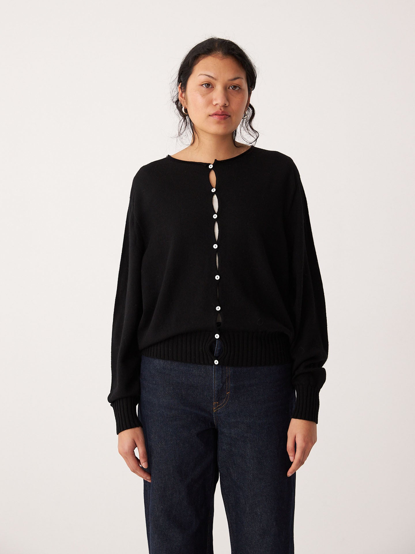 A person faces forward against a plain light background, wearing the Francie Anni Cardigan in black with dark blue jeans.