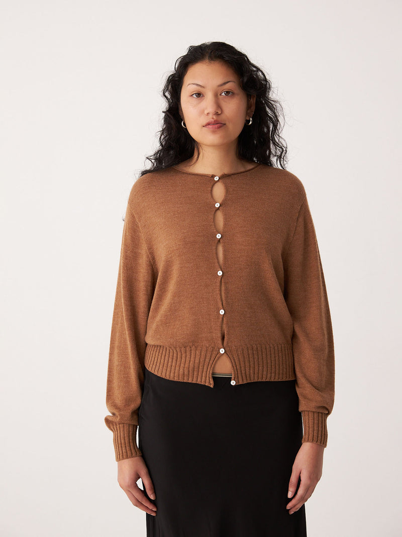 A person with long, wavy hair wears Francie's Anni Cardigan in Brown Sugar and a black skirt, standing against a plain white background.